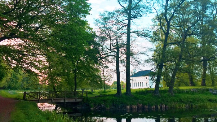 En smuk park med en lille bro og et hus i baggrunden