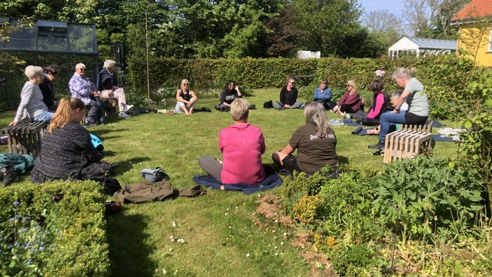 En gruppe af mennesker sidder ude på en grønne eng og samtaler.