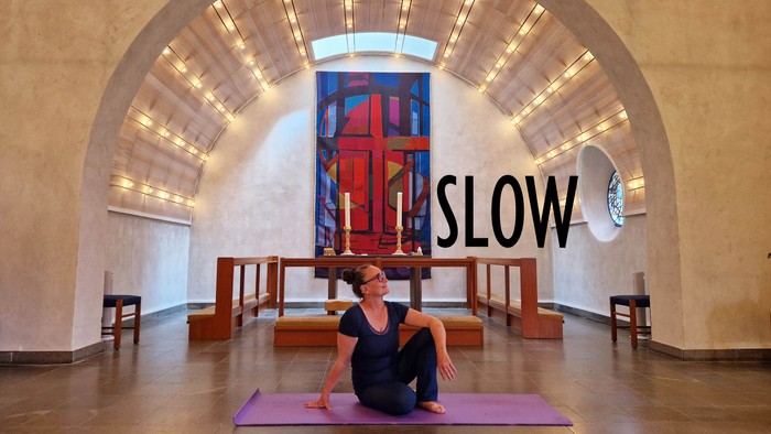 Kvinde i yoga-pose på rosa yoga-mat i indendørs rum med stor farverig glasmosaik.