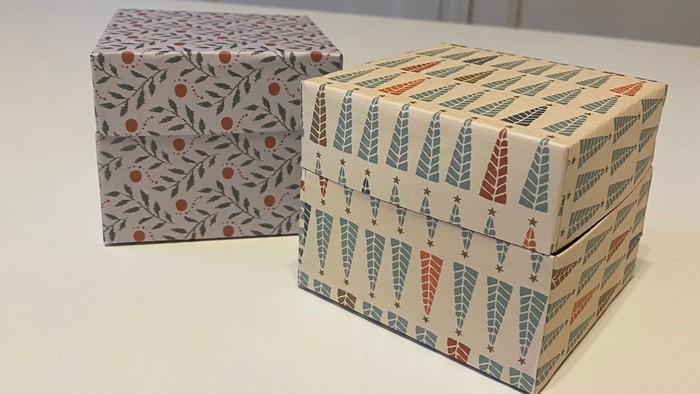 Dekorative gaveæsker med festlige julemønstre, den ene med bær og den anden med juletræer.