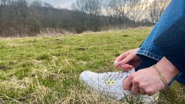 Person binder hvide sneakers med gule detaljer på en græsklædt mark udendørs.