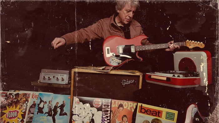 Musiker, der spiller på elektrisk guitar omgivet af vintage-plader, bånd og memorabilia.