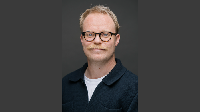 En mand med briller og overskæg iført en mørk jakke over en hvid skjorte.