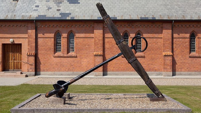 En stor jernanke udstillet på græsplæne forud for et rødt murstensbygning.