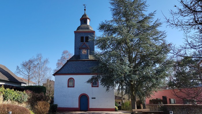 Idyllische weiße Kirche mit Glockenturm in einer ruhigen, landschaftlich gestalteten Dorfgegend.