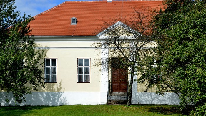 Ein weißes Haus mit rotem Dach und grünem Rasen vor einem klaren blauen Himmel.
