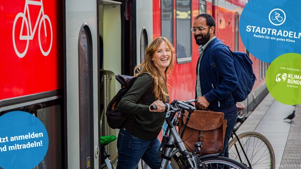 Zwei Personen mit Fahrr�dern in der N�he eines Zuges, die stadtfreundliches Radfahren und Klimaschutzprogramme f�rdern.