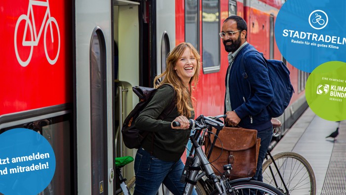 Zwei Personen mit Fahrrädern in der Nähe eines Zuges, die stadtfreundliches Radfahren und Klimaschutzprogramme fördern.