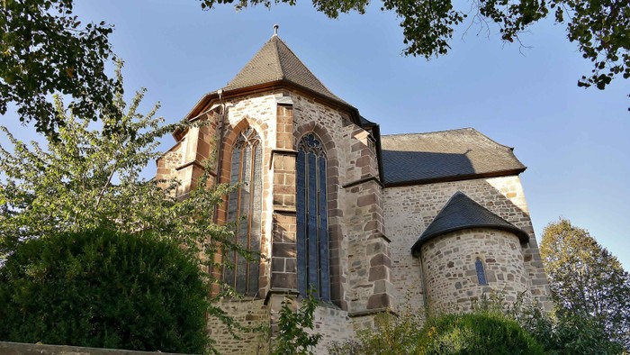 Alte Steinkirche mit hohen Fenstern und einem kleinen Turm, umgeben von Grünflächen.