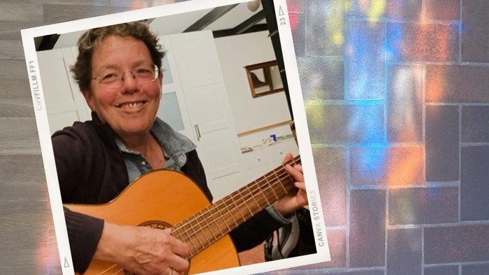 Eine fröhliche Person spielt drinnen eine akustische Gitarre, während im Hintergrund ein farbenfroher, prismenartiger Lichteffekt zu sehen ist.