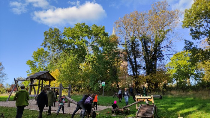 Jugendliche und Kinder toben auf einem Spielplatz. Im Hintergrung ist die Kirchenruine Lichtenberg zu erkennen.