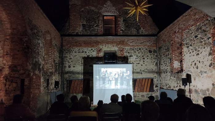 Menschen sitzen in der dunklen Kirchenruine Lichtenberg und schauen einen Film, der auf eine Leinwand projeziert wird.