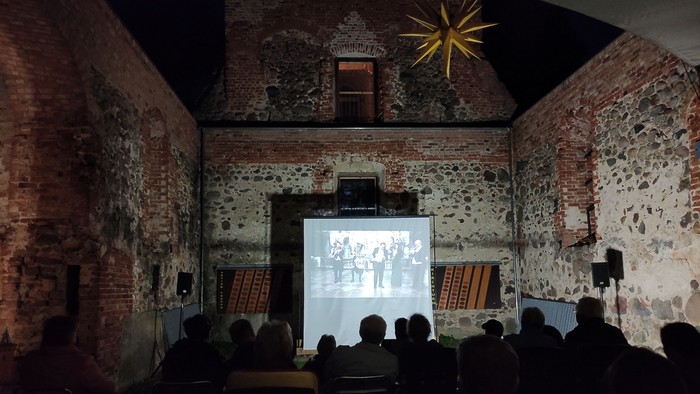 Menschen sitzen in der dunklen Kirchenruine Lichtenberg und schauen einen Film, der auf eine Leinwand projeziert wird.