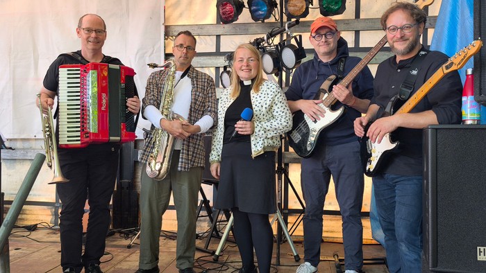 Pfarrerin inmitten einer Musikgruppe mit Akkordeon und Gitarren.
