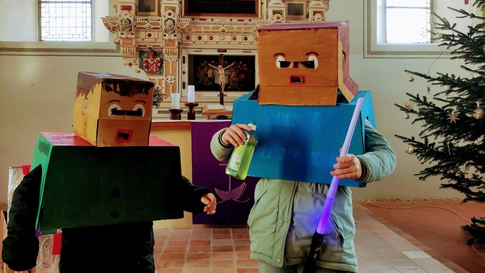 Zwei mit Kartons kostümierte Kinder vor einem Altar während eines Anspiels.
