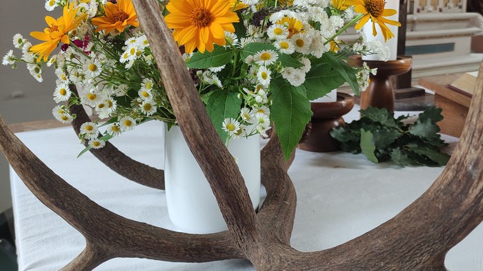Ein Geweih und Blumen liegen auf einem weiß gedeckten Tisch vor einem Altar.