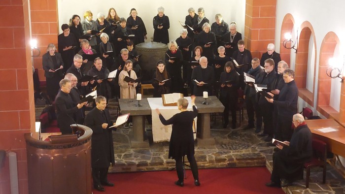 Ein Chor singt in einer Kirche, begleitet von einem Dirigenten.