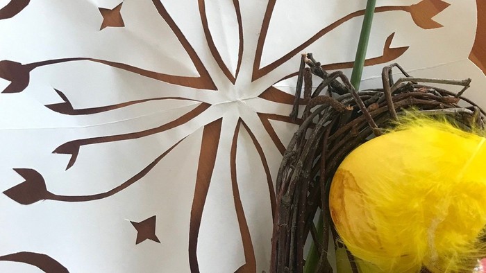 Dekorativt papirsparasol med blomstermønster, der holder en kurv af flettet vidje med en gul blomst og et æg.