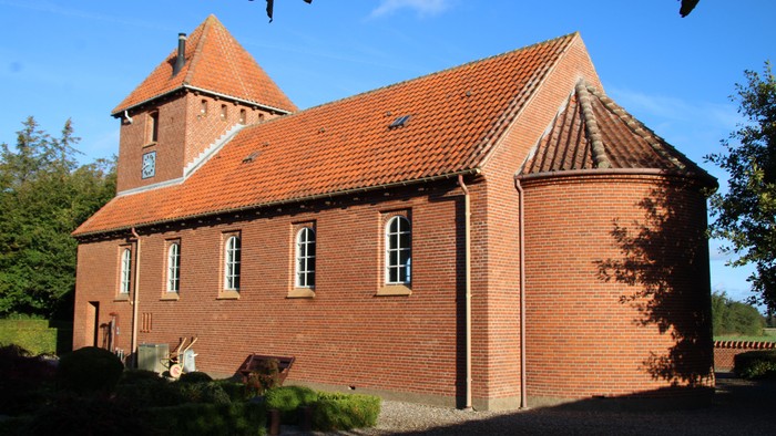 Røde murstensbygning med spiret og fladt tag i røde tegl.