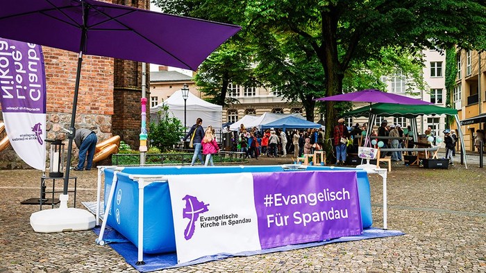 Wasserbecken vor der Kirche mit Banner "Evangelisch Für Spandau" auf Tauffest