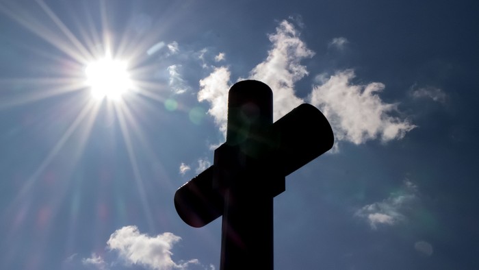 Ein Kreuz vor einem sonnenstrahl durchzogenen Himmel