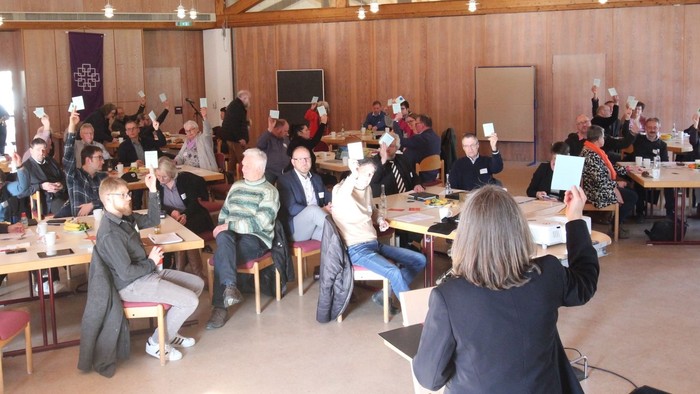 Ein großer Raum mit vielen Menschen an Tischen, einige sitzen, andere stehen und reden.