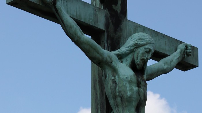 En bronzer statue af Jesus på korset mod en klar blå himmel.