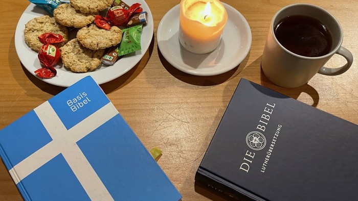 Gemütlicher Aufbau mit Gebäck, Kerzen, Kaffee und zwei verschiedenen Bibeln auf einem Holztisch.
