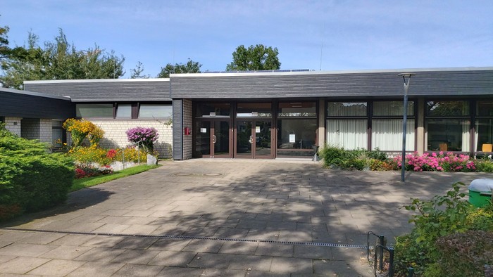 Das Bild zeigt ein modernes Gebäude mit großen Fenstern und einem gepflegten Garten.