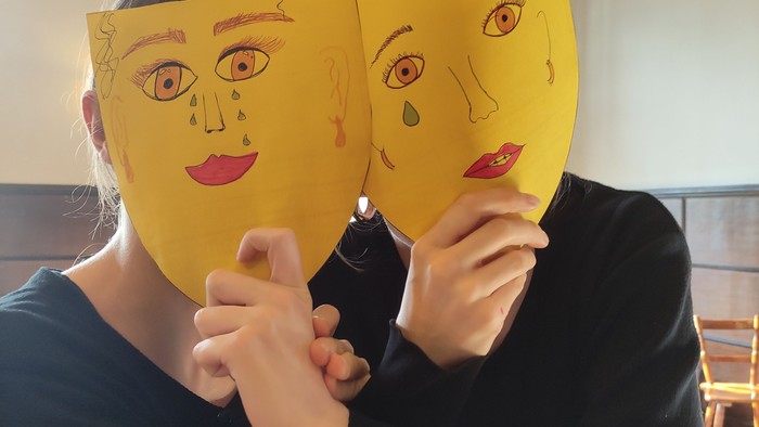 Zwei Jugendliche halten sich gegenseitig eine Maske vors Gesicht. Die Masken sind selbst gemalt und aus den Augen laufen Tränen.