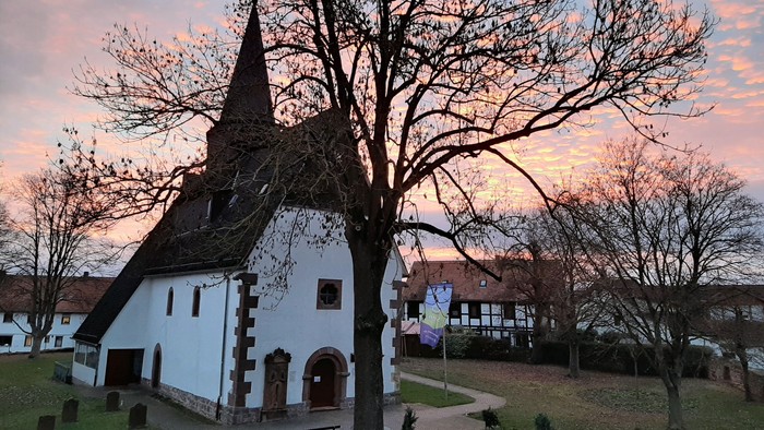 Kirche mit Turmspitze und kahlen Bäumen bei Sonnenuntergang