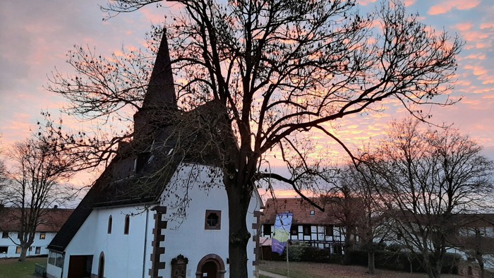 Kirche mit Turmspitze und kahlen Bäumen bei Sonnenuntergang
