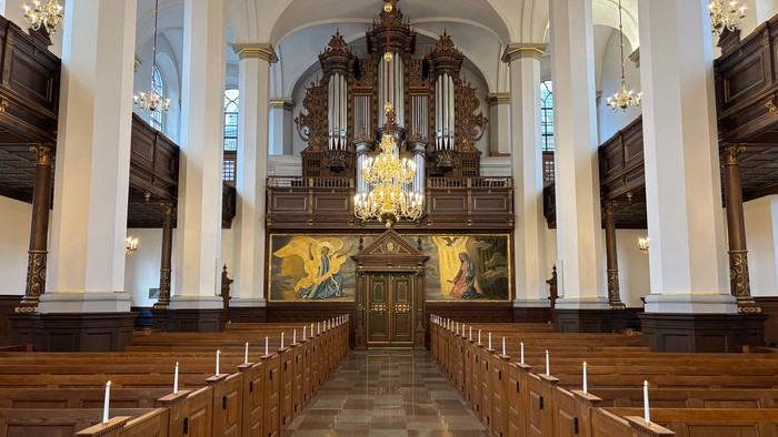 Elegant kirkeinteriør med stort orgel, træbænke og prægtige lysekroner.