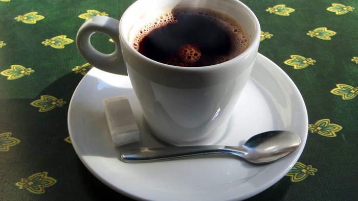 En lille kaffekop på en underduk med gule mønstre