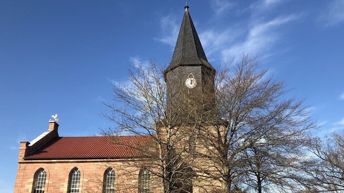 Kirchturm mit Uhr und Kirche im Hintergrund unter blauem Himmel