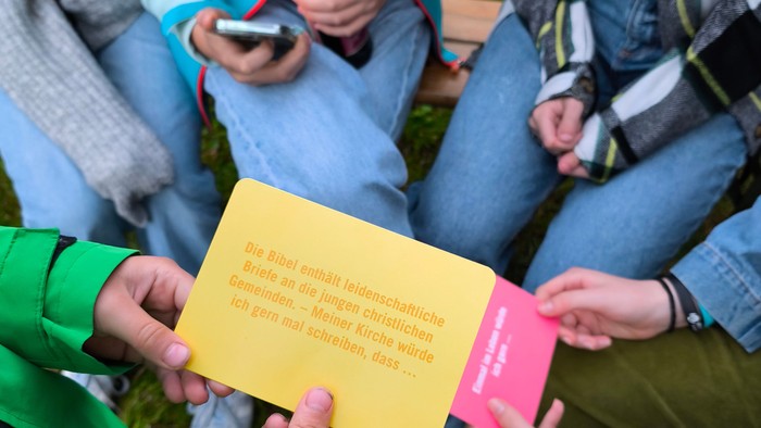 Jugendliche sitzen im Kreis, zwei halten eine Aktionskarte.