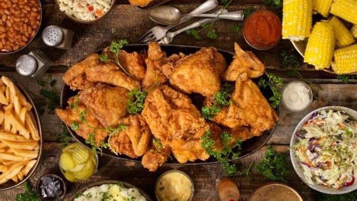 Un généreux festin composé de poulet frit, de maïs, de salade de chou, de frites, de haricots et de sauces à tremper, présenté sur une table en bois rustique.