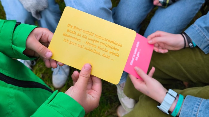 Jugendliche sitzen im Kreis, zwei halten eine Aktionskarte.