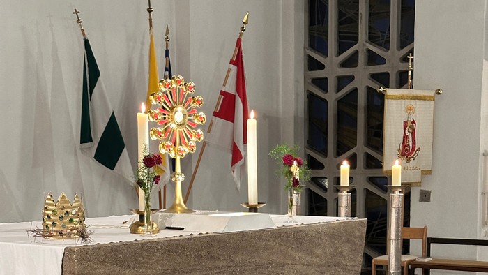 Eleganter Kirchenaltar, geschmückt mit Kerzen, Fahnen, Blumengestecken und religiösen Verzierungen auf einem Marmorboden.