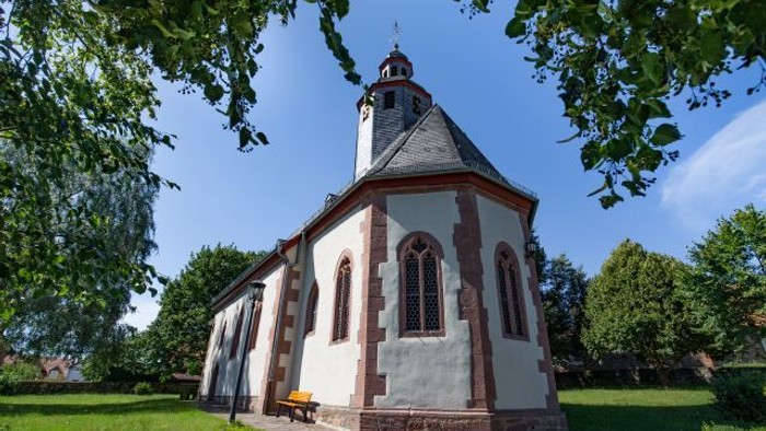 Idyllische Kirche mit weiß-rotem Backsteinfassade, umgeben von üppigem Grün unter einem klaren Himmel.
