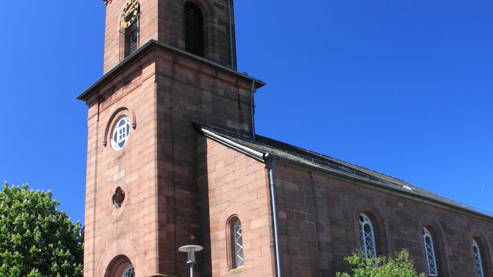 Kirche mit hohem Uhrturm und Spitzhelm vor klarem blauen Himmel.