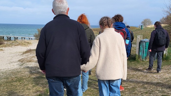 Gruppe af mennesker, der går langs en kyststi nær havet på en klar dag.