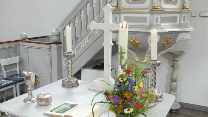 Eleganter Kirchenaltar mit Kerzen, Blumenschmuck und religiösen Büchern auf einem weißen Tisch.