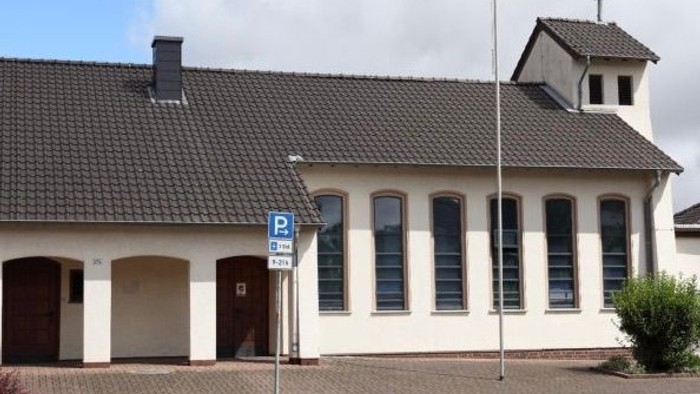 Das Bild zeigt ein weißes Gebäude mit schwarzem Dach und einem Parkplatzschild davor.