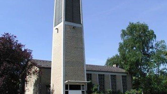 Kirchturm mit Kreuz vor Kirche und Bäumen