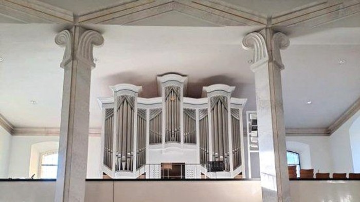 Elegante Kircheninnenausstattung mit einer großen Pfeifenorgel, die auf klassischen Säulen erhöht steht, sowie gestuften Sitzreihen und Kirchenbänken.