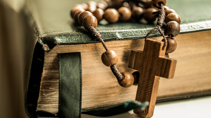 Ein hölzernes Kreuz und Rosenkranz auf einem grünen Buch