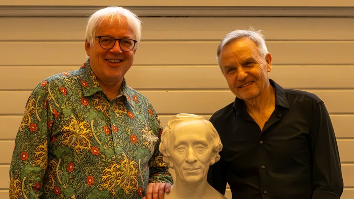 To mænd poser med en buste-skulptur mellem sig og smiler til kameraet.