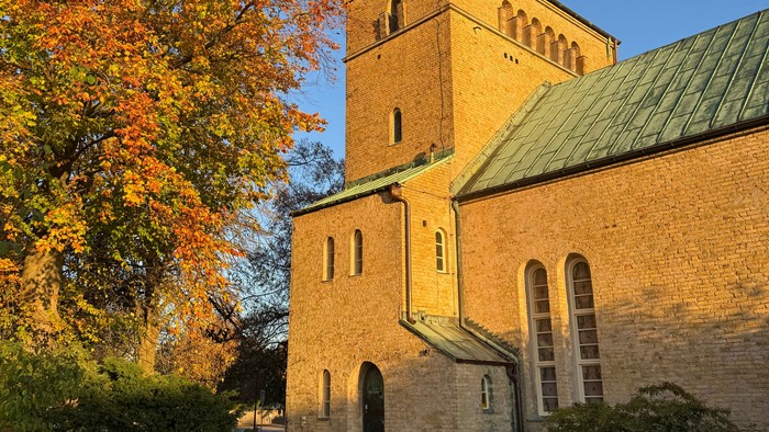 Historische Steinkirche, umhüllt von warmem Herbstsonnenlicht, umgeben von goldenem Laub.