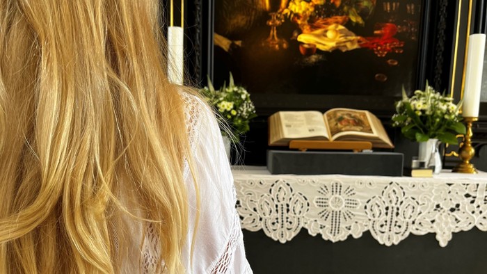 En kvinde med blond hår ser i et spejl med maleri og blomster.